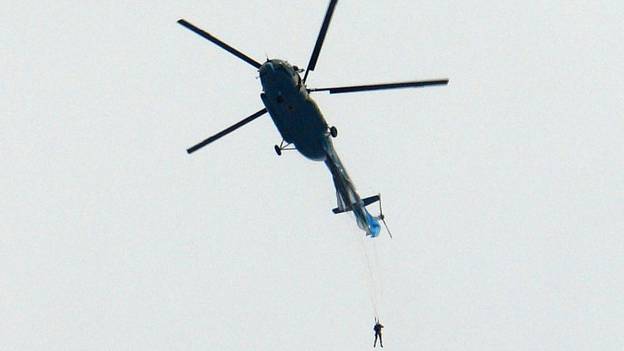 慢胎陷入困境后，跳伞运动员从直升机悬挂着