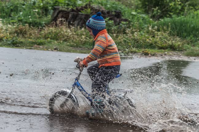 暴风雨过后，男孩骑着自行车穿过水坑。（信用：Unsplash/Vitolda Klein）