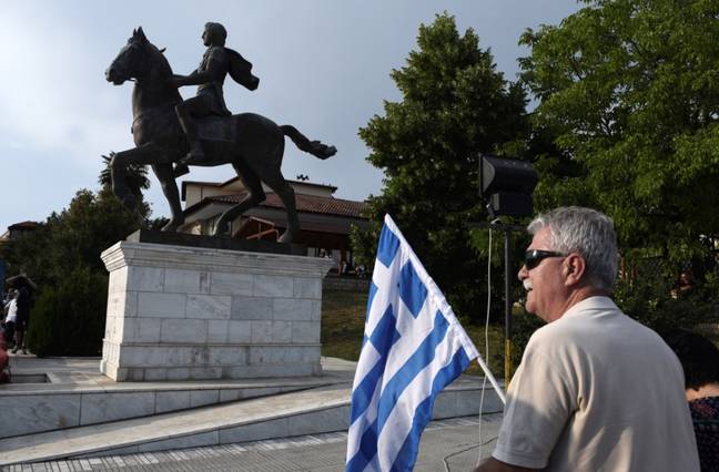 一名男子在亚历山大大帝的雕像旁举着一面希腊国旗。信贷:爸爸